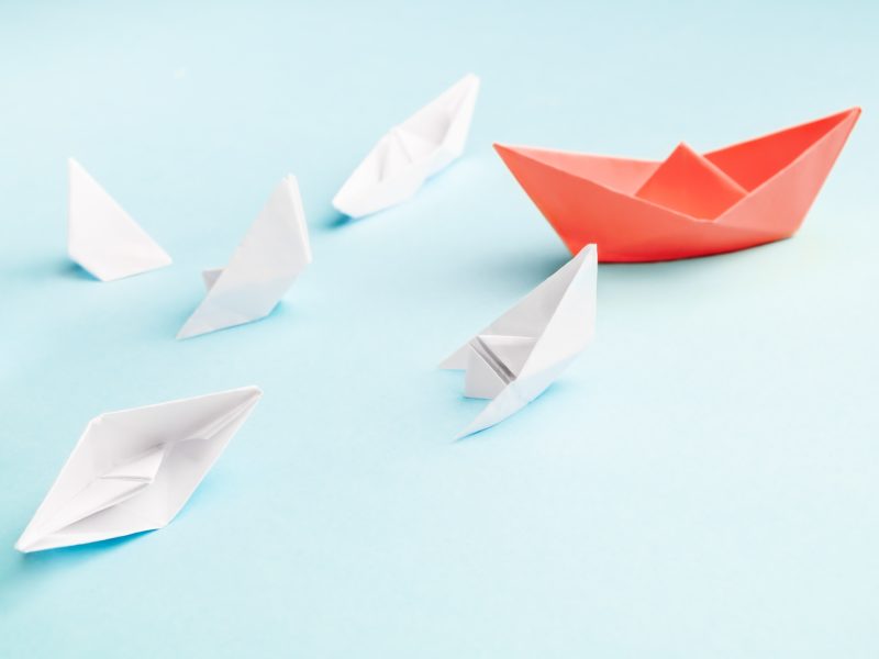 Unsuccessful leadership concept. Red paper boat and a lot of sinking ships
