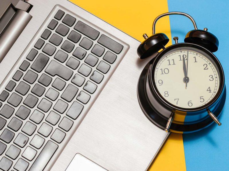 Alarm clock with a laptop on a yellow and blue background.